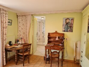 A cozy room with a wooden table, two chairs, a radiator, a painting, and a door leading to another room. - Room Châteauneuf: Rustic Charm with Private Terrace and Wifi in Saint-Benoît-sur-Loire (Saint-Benoît-sur-Loire)