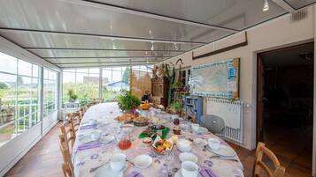 Een eethoek met een ronde tafel gedekt voor een maaltijd, omringd door stoelen, met uitzicht op groen buiten.