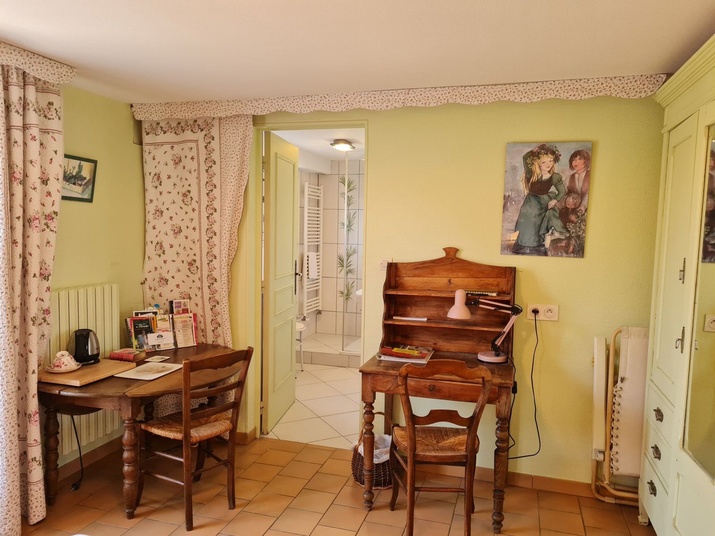 Een gezellige kamer met een houten tafel, twee stoelen, een radiator, een schilderij en een deur naar een andere kamer.