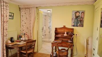 Een gezellige kamer met een houten tafel, twee stoelen, een radiator, een schilderij en een deur naar een andere kamer.