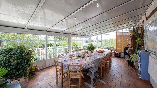 Une terrasse couverte avec une table à manger dressée pour un repas, entourée de chaises, et donnant sur un jardin.