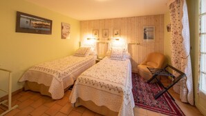 Une chambre avec deux lits simples, une chaise, une petite table et une fenêtre avec des rideaux.