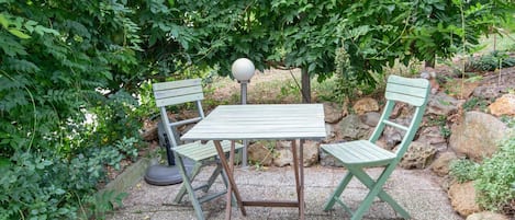 Une terrasse de jardin avec une table et deux chaises, entourée de verdure et de rochers.