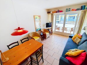 Ein Wohnzimmer mit einem Holzesstisch, Korbstühlen, einem blauen Sofa und einer roten Pendelleuchte.