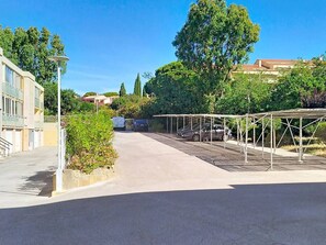 Ein Parkplatz mit überdachtem Carport, ein Gebäude mit Flachdach und Grünflächen.