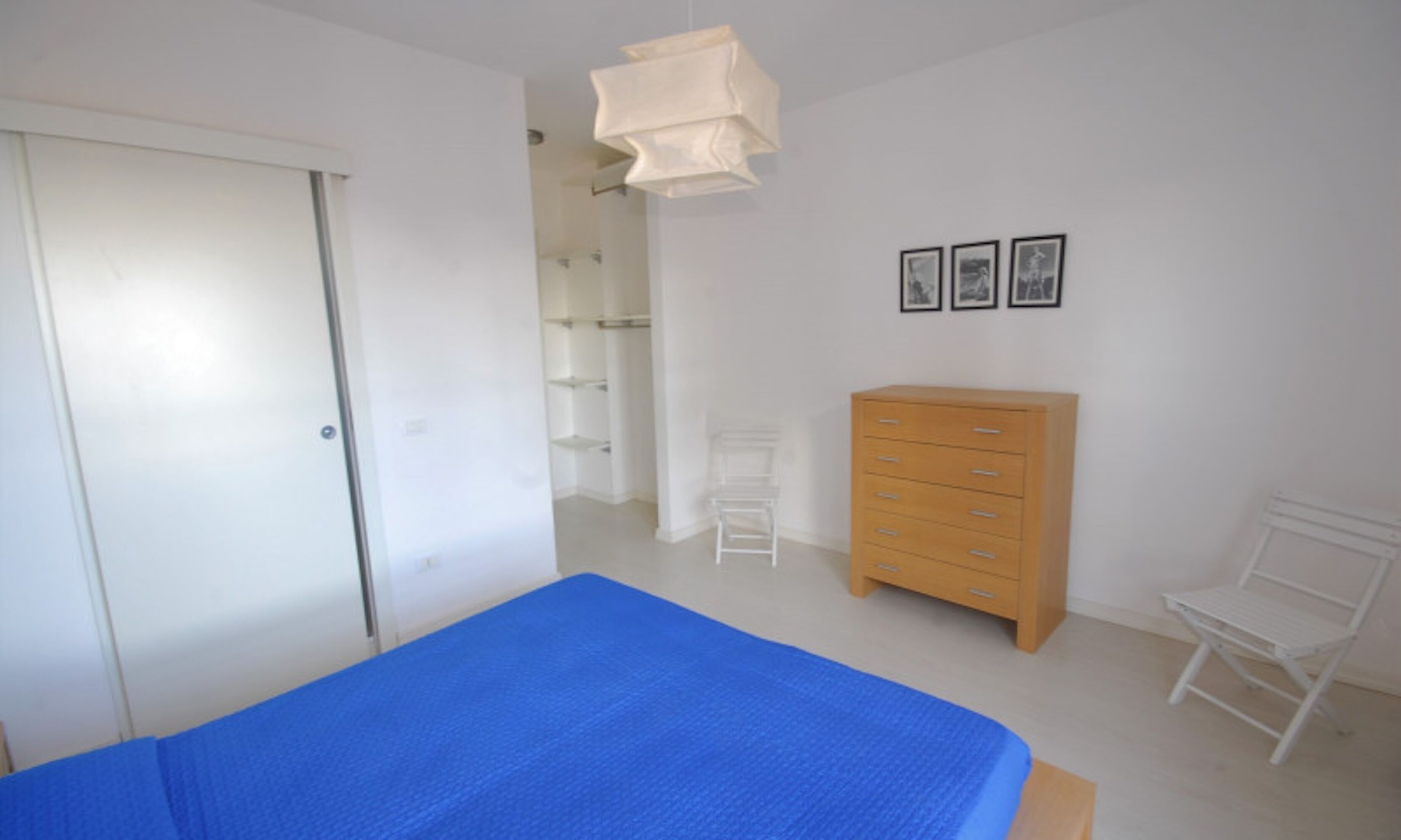 Ein Schlafzimmer mit einem Bett, einer Holzkommode, einem weißen Stuhl und einem Kleiderschrank.