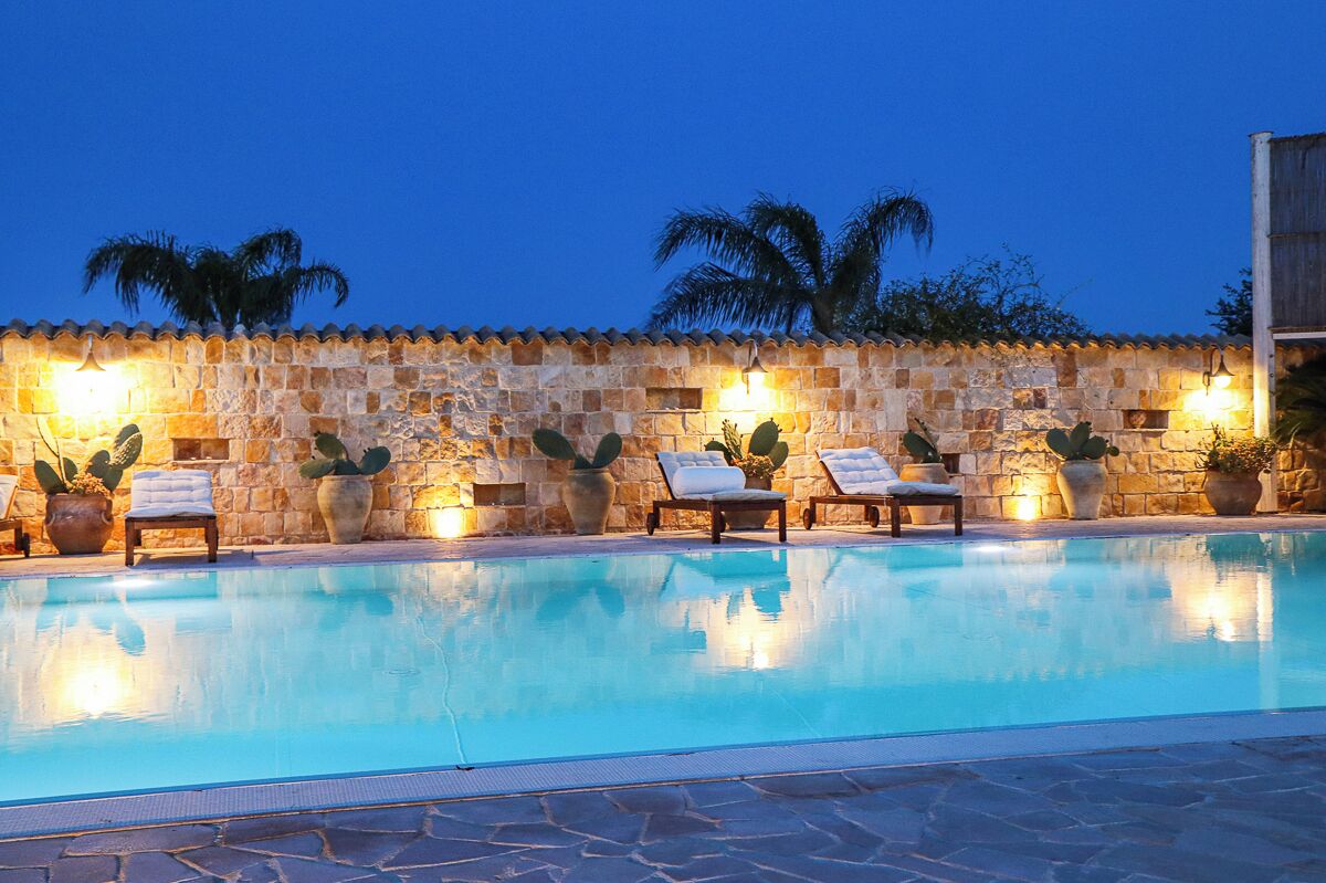 Una piscina con paredes de piedra y cactus, rodeada de sillas de descanso y plantas en macetas.