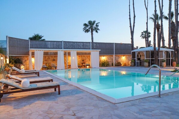 A pool area with lounge chairs, a covered seating area, and palm trees. - Villa Erika SicilyMyHome (Ispica)