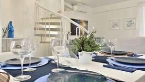A dining table set with blue plates, clear wine glasses, and a white vase with green foliage. - Casa Blanca a due Passi dal Mare (Ispica)