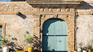A stone building with a large arched door, potted plants, and a decorative stone architrave. - Casa Blanca a due Passi dal Mare (Ispica)