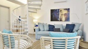 A modern living room with a spiral staircase, a light blue sofa, and wicker chairs. - Casa Blanca a due Passi dal Mare (Ispica)