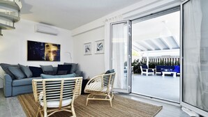 A modern living room with a sofa, two wicker chairs, a large window, and a view of an outdoor seating area. - Casa Blanca a due Passi dal Mare (Ispica)
