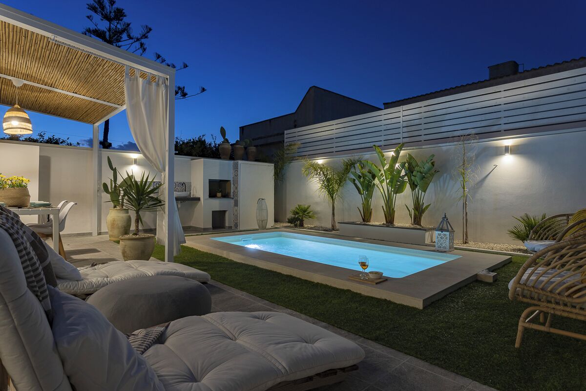 A backyard with a swimming pool, outdoor seating, and potted plants.