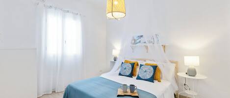 Et soveværelse med seng, sengeborde, en hængende lampe og et vindue med gardiner.