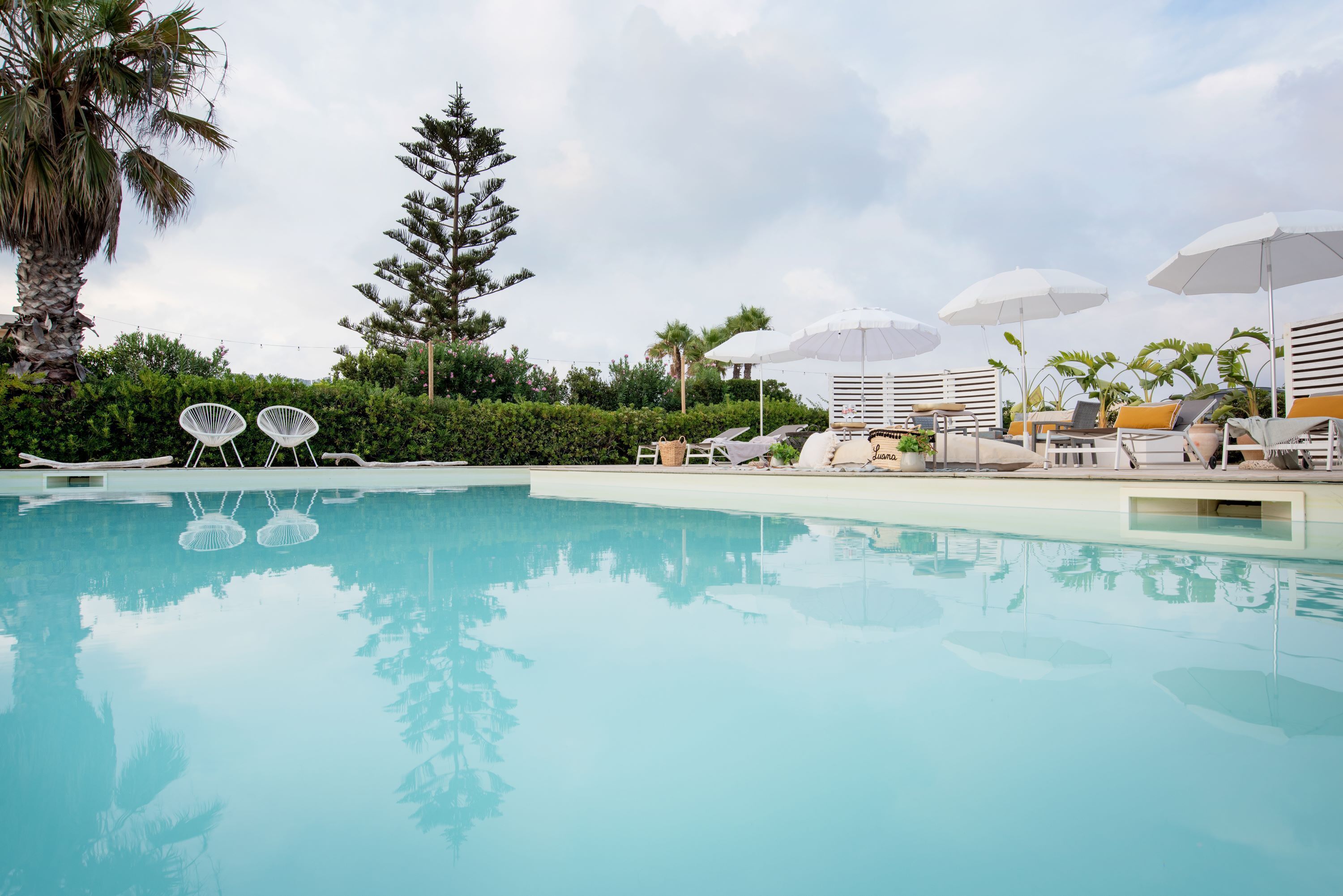 A swimming pool with lounge chairs and umbrellas, surrounded by greenery and palm trees.
