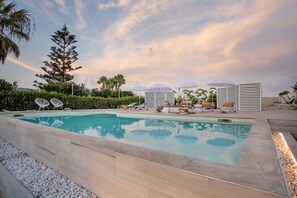 A swimming pool with lounge chairs and umbrellas, surrounded by greenery and palm trees. - Villa Elysian con Piscina Privata (Pachino)