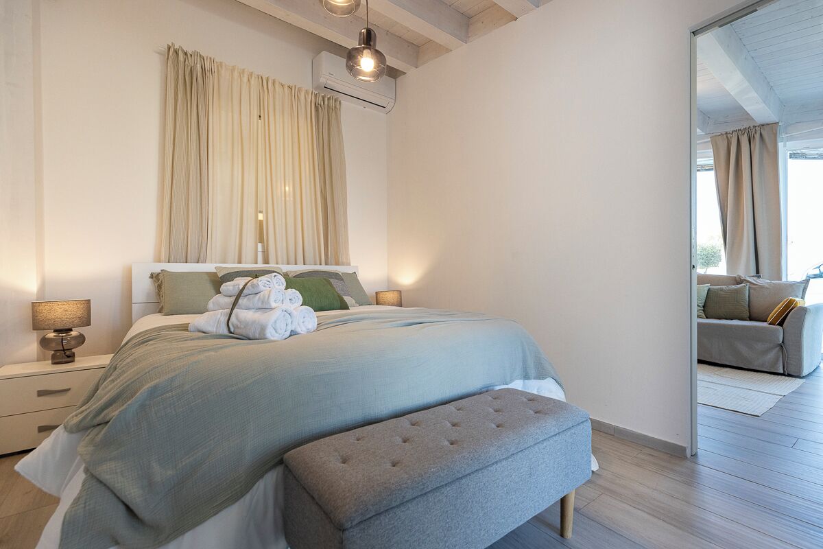 Een slaapkamer met een bed, nachtkastjes, een bankje en uitzicht op een andere kamer.