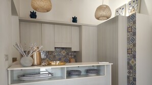 A modern kitchen with white cabinets, a white countertop, and a bar area with two stools. There are decorative items on the counter, including a vase with branches and a bowl. - Villa Elysian con Piscina Privata (Pachino)
