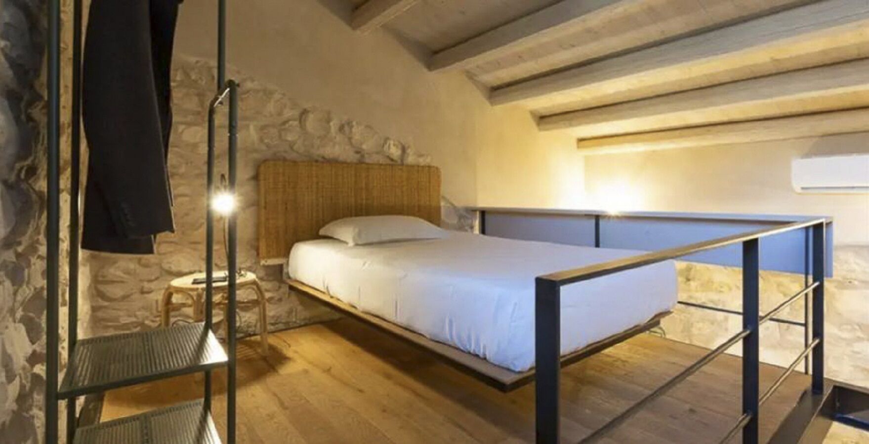 Ein Einzelbett mit hölzernem Kopfteil in einem Raum mit Steinwänden und Holzboden.