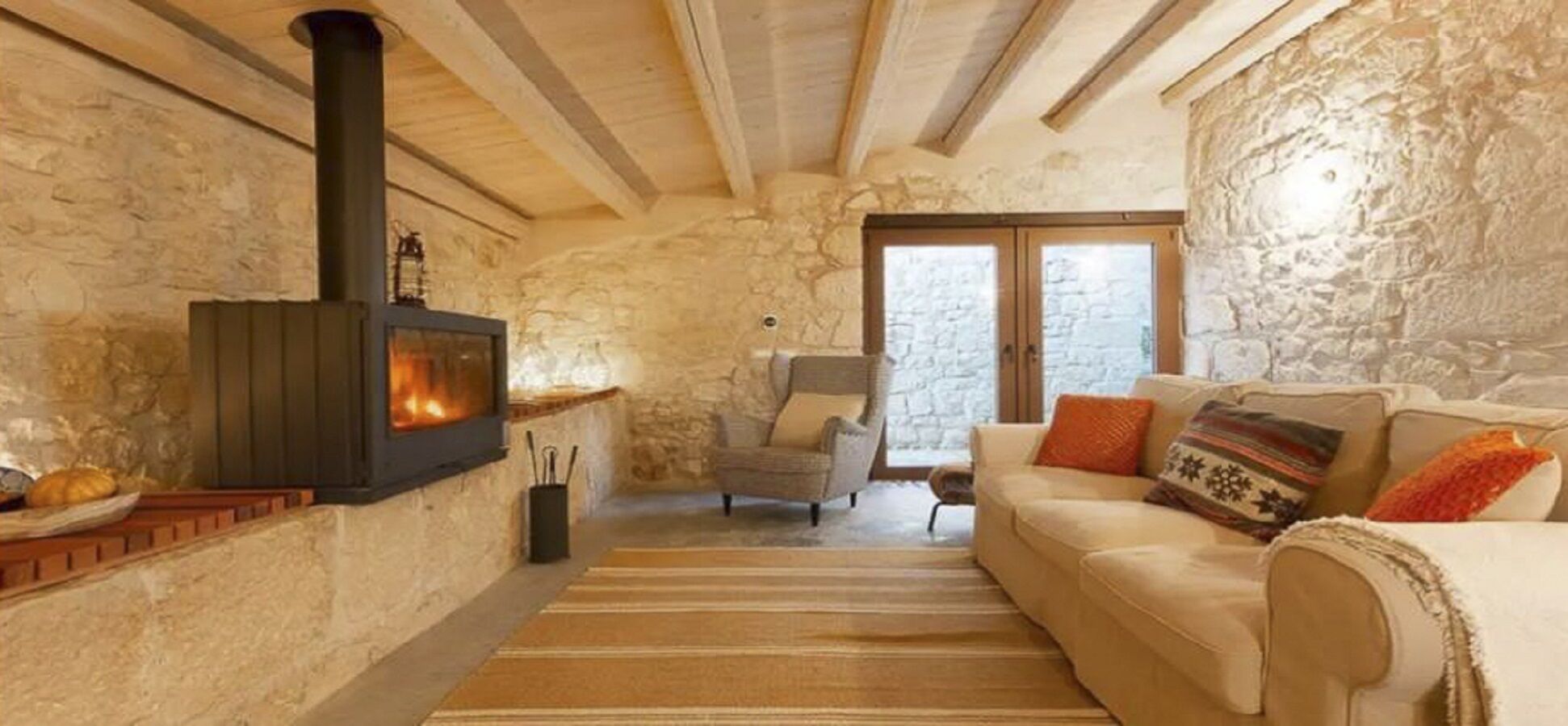 A cozy room with a stone wall, a fireplace, a sofa, and a chair.