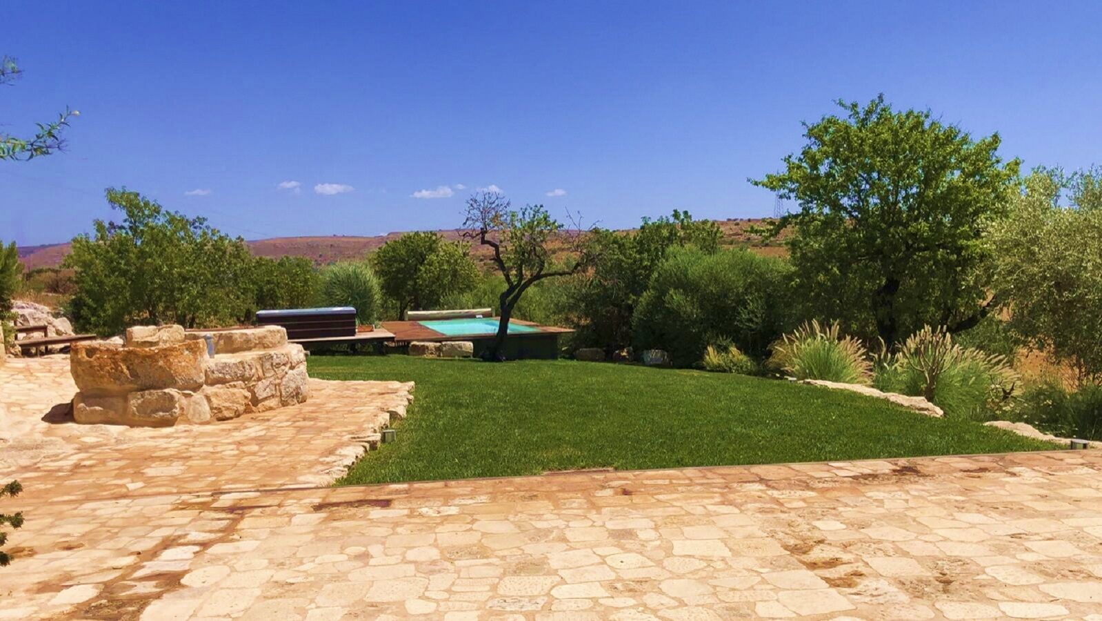 A patio area with stone flooring, a swimming pool, and a well-maintained lawn.