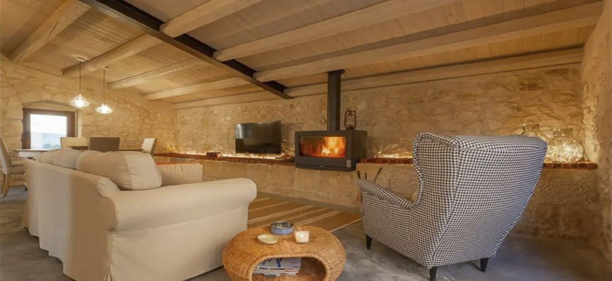 A cozy room with a sofa, armchair, and a small round table with candles. A fireplace is visible in the background.