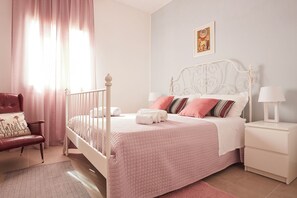 A neatly arranged bedroom with a white bed, pink bedding, a white nightstand, and a red chair. - Villa Zamia SicilyMyHome      (Ispica)