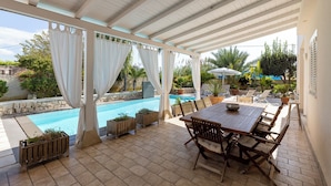 A covered outdoor area with a pool, patio furniture, and potted plants. - Villa Zamia SicilyMyHome      (Ispica)