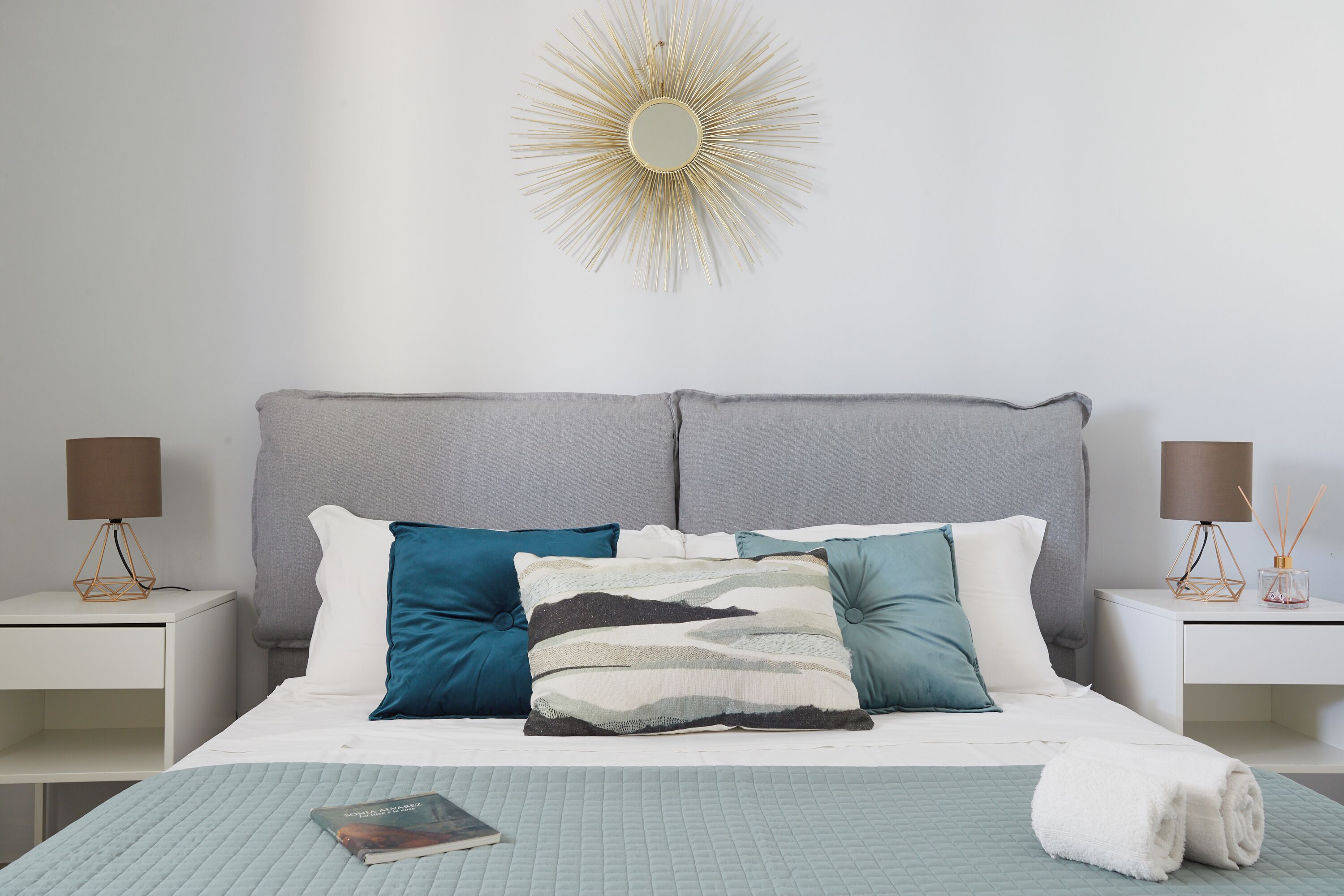 A neatly made bed with a quilted blue bedspread, multiple pillows in various colors, and a white towel on the side.