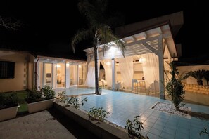 A modern house with a covered patio area, potted plants, and a well-lit interior. - Sicily Sun con Accesso Alla Spiaggia (Ispica)
