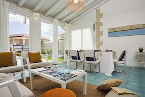 A spacious living area with a white sofa, a coffee table with magazines, and a dining area with chairs and a table. - Sicily Sun con Accesso Alla Spiaggia (Ispica)
