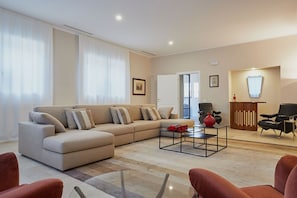Ein modernes Wohnzimmer mit einem beigefarbenen Sofa, einem Glastisch und roten Akzenten.