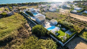 Vue aérienne d’un quartier résidentiel situé sur la côte, avec des maisons, une piscine et une vue dégagée sur la mer.