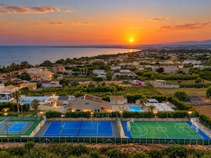 Un quartier résidentiel avec des maisons, un court de tennis et une vue sur le coucher de soleil en mer.