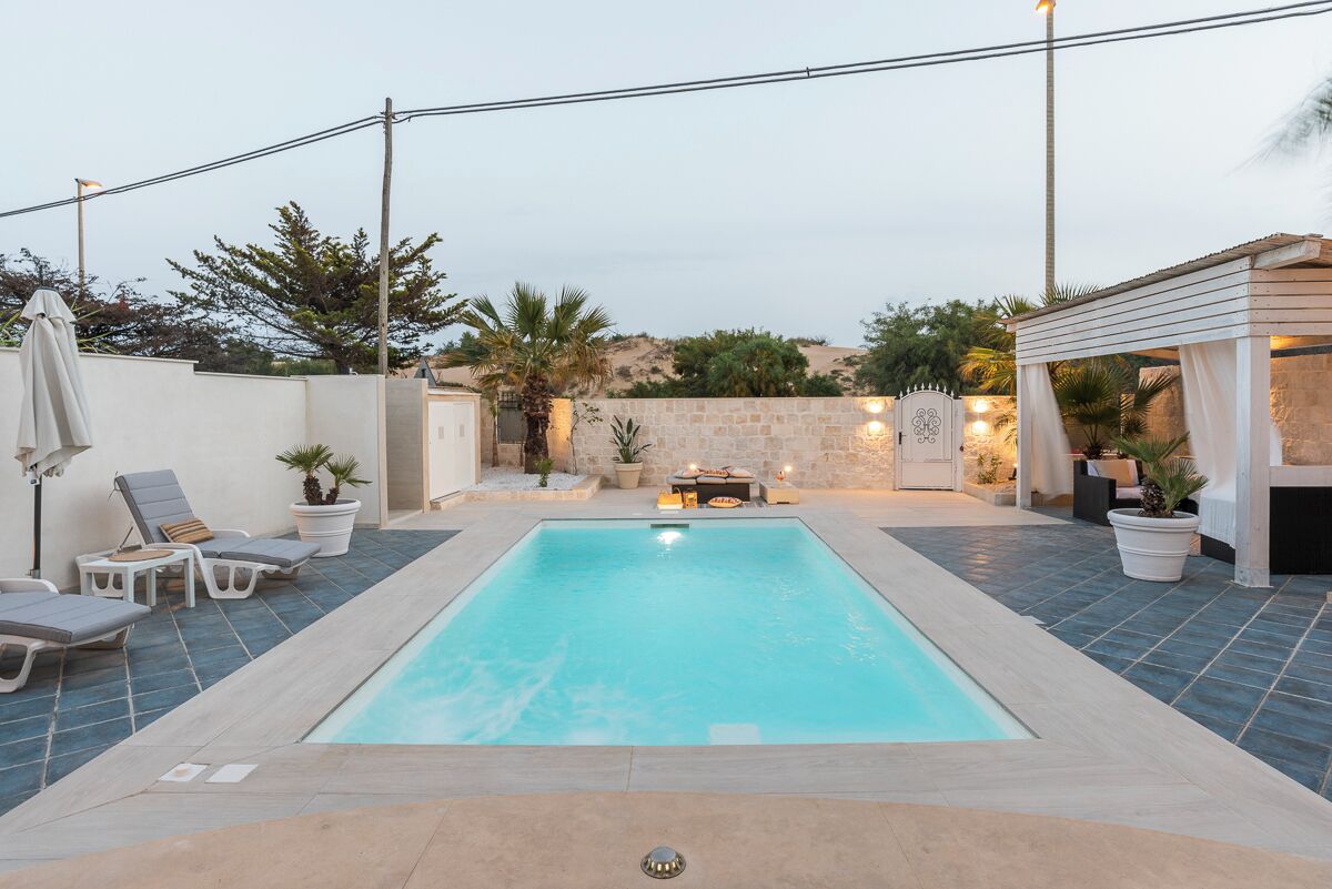 Una piscina rectangular con sillas de descanso y plantas en macetas alrededor.