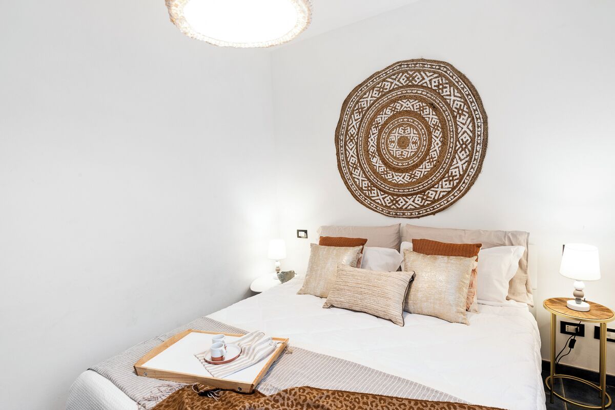 Une chambre à coucher bien rangée, avec un grand lit, une décoration murale et une table de chevet sur laquelle se trouve une lampe.