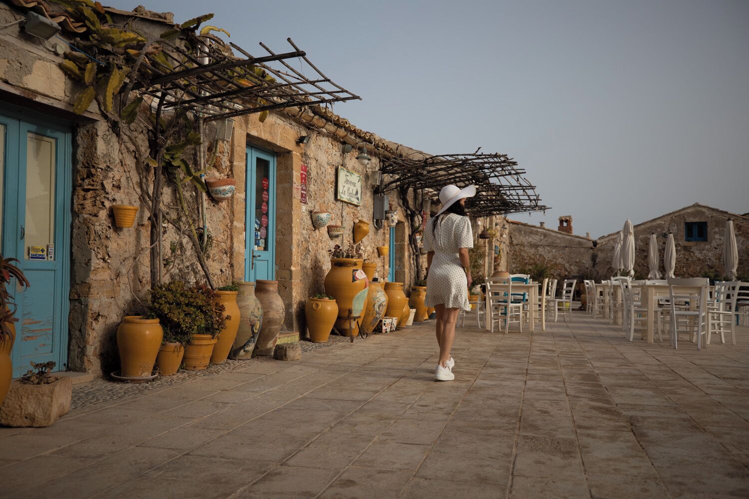 Un bâtiment en pierre, orné de pots en terre cuite, avec une porte bleue et des sièges à l’extérieur.