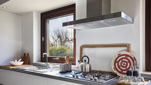 A modern kitchen with a gas stove, stainless steel appliances, and a window with a view of trees. - Villa Scarlet con Piscina Privata (Modica)