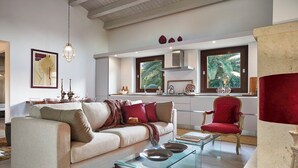 A modern living room with a sofa, coffee table, and red armchair. A kitchen with a window and a red chair is visible in the background. - Villa Scarlet con Piscina Privata (Modica)