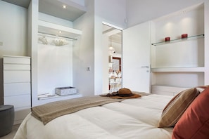 A modern bedroom with a bed, a wardrobe, a mirror, and a shelf with decorative items. - Villa Scarlet con Piscina Privata (Modica)