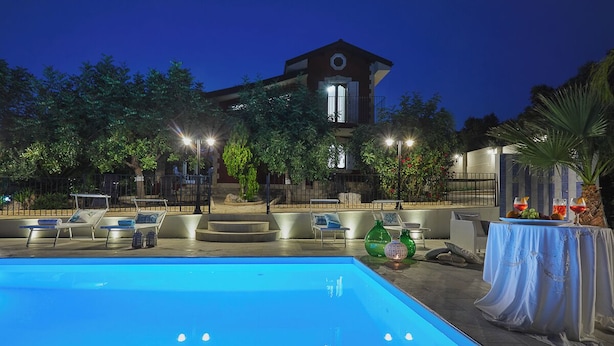 A swimming pool with lounge chairs, a table with drinks, and a building in the background. - Villa del Colle con Piscina Privata (Ispica)