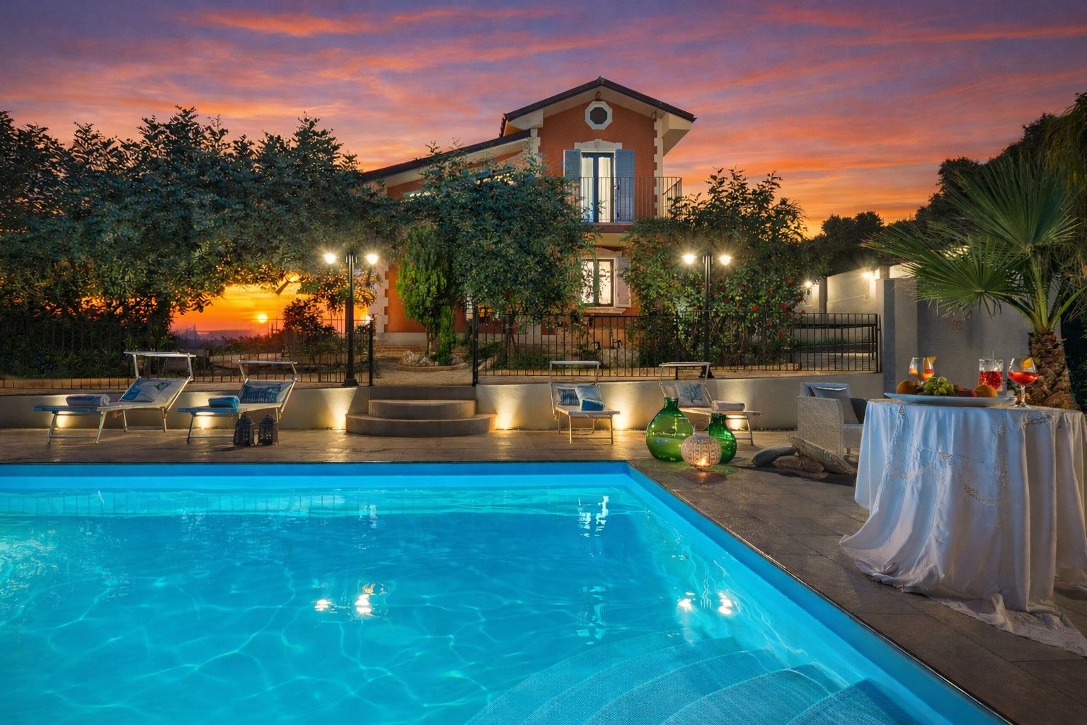Ein Swimmingpool mit Liegestühlen, ein Tisch mit Getränken und ein Gebäude mit Balkon.