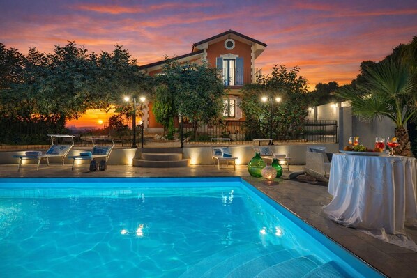 Ein Swimmingpool mit Liegestühlen, ein Tisch mit Getränken und ein Gebäude mit Balkon.