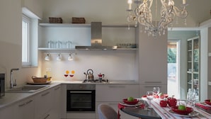 Una cocina moderna con armarios blancos, horno empotrado y comedor con mesa dispuesta para una comida.