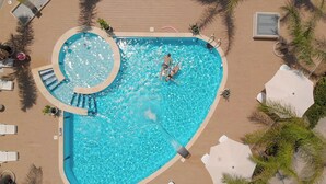 An aerial view of a swimming pool with a circular section, surrounded by lounge chairs and palm trees. - Attico Vista Mare SicilyMyHome (Ispica)