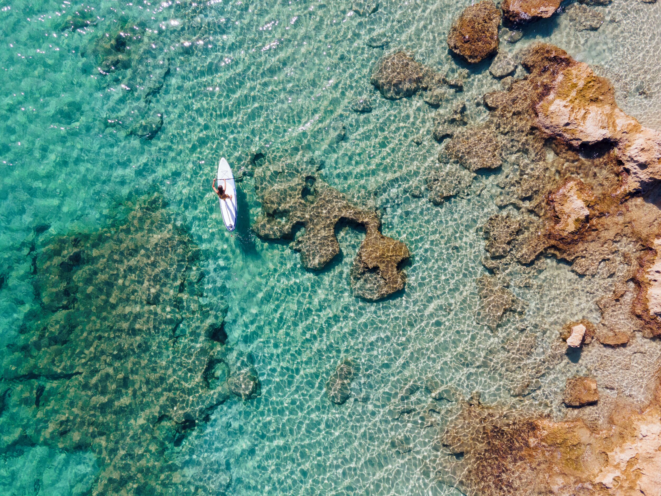 Mar turquesa cristalina con costa rocosa y un barco blanco solitario.