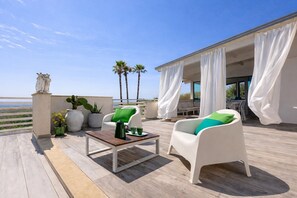 Una terraza con mobiliario blanco, una mesa y plantas en macetas.