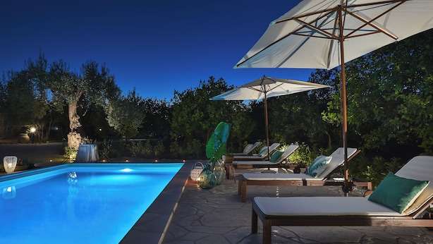Une piscine entourée d’arbres et dotée d’un sol en pierre, avec des chaises longues et des parasols à proximité.