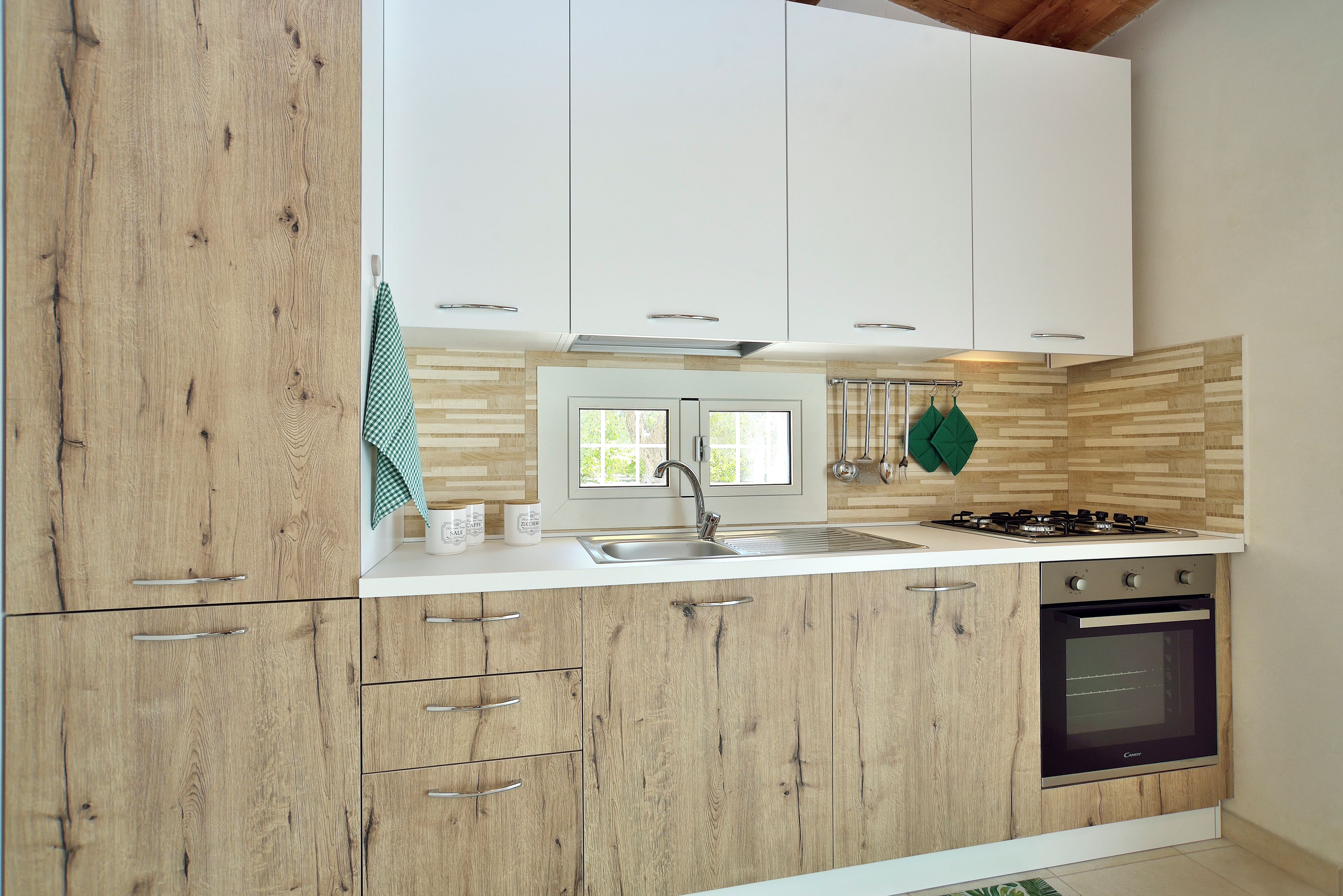 A modern kitchen with wooden cabinets, a white countertop, a stainless steel sink, a gas stove, and a built-in oven.