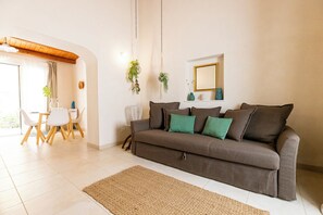 Una sala de estar con un sofá marrón, un tapete tejido y un comedor con mesa y sillas blancas.